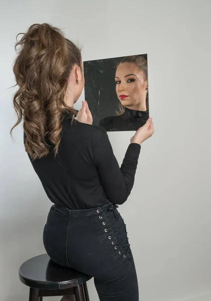 黒のブラウスと赤い唇の魅力的な女性は 背景の前に鏡を見てください ブドアのシーンだ カメラの前で身に着けている長い巻き毛と黒のジーンズを持つ官能的な若い女性 — ストック写真