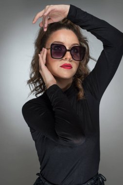 Gri arka planda siyah bluzlu ve güneş gözlüklü bir kadın. Kırmızı dudaklı güzel bir kız. Güneş gözlüklü çekici bir kadının portresi. Kameraya bak.