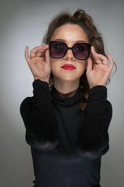 stock image Woman with sunglasses  and black blouse against a grey background. Style beauty girl with red lips.Portrait of stunning young woman in sunglasses look into the camera