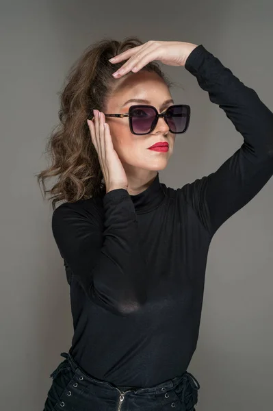 Vrouw Met Zonnebril Zwarte Blouse Tegen Een Grijze Achtergrond Stijl — Stockfoto