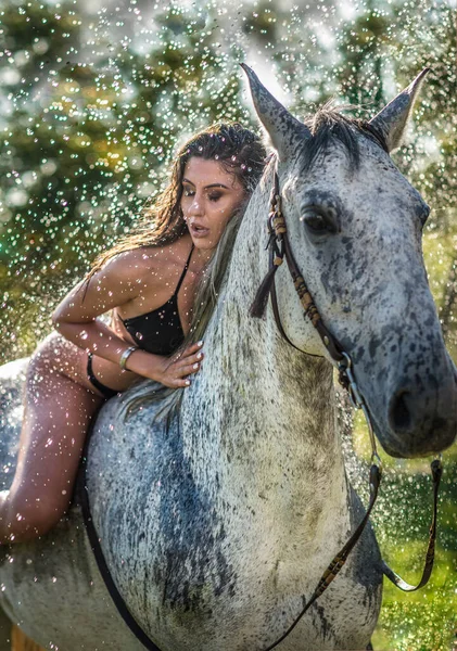 美丽的黑发女人 黑色比基尼和白色衬衫骑在水滴下的白马上 一个性感迷人的女孩和一匹马在农场里嬉戏玩耍 — 图库照片
