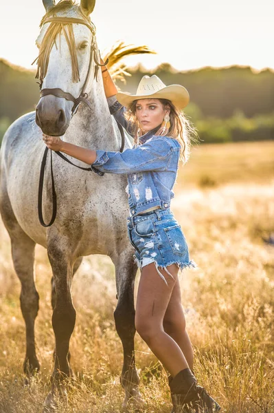 美丽的金发女人 卷曲的头发 戴着白帽 骑着马 一个穿着斜纹棉布和马的女孩的画像 美丽的女孩在农场里和一匹马交流和玩乐 — 图库照片
