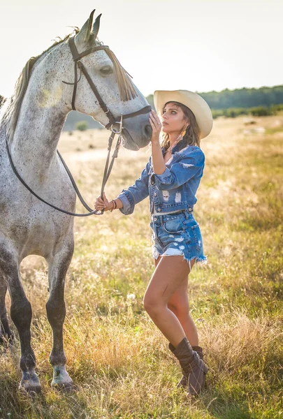 美丽的金发女人 卷曲的头发 戴着白帽 骑着马 一个穿着斜纹棉布和马的女孩的画像 美丽的女孩在农场里和一匹马交流和玩乐 — 图库照片
