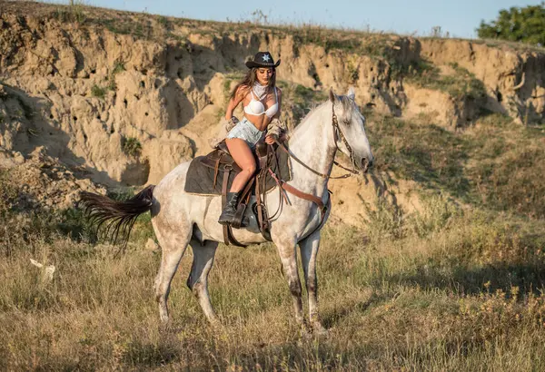 砂漠で馬に乗った帽子を持つセクシーなカウガール 馬に乗ったカウボーイ帽子の美しい女の子 山で馬に乗った美しいカウガール アウトドアライフスタイルの肖像 ロイヤリティフリーのストック画像