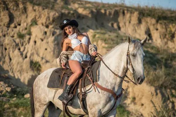 砂漠で馬に乗った帽子を持つセクシーなカウガール 馬に乗ったカウボーイ帽子の美しい女の子 山で馬に乗った美しいカウガール アウトドアライフスタイルの肖像 ロイヤリティフリーのストック写真