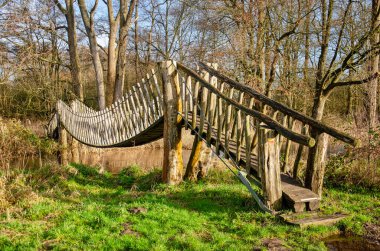 Oisterwijk, The Netherlands, January 15, 2023: wooden suspension bridge for hikers across a small creek in a landscape with grass and trees