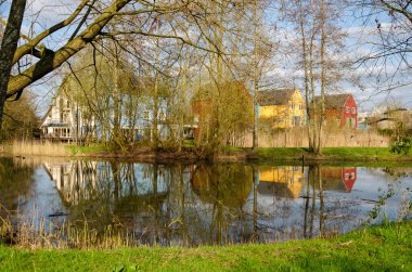 Culemborg, Hollanda, 8 Nisan 2023: yeşil bir çevrede ahşap cepheli renkli evler baharda bir gölete yansıyor.