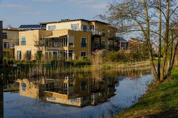 Stock image Culemborg, The Netherlands, April 8, 2023: wooden housing block in Lanxmeer neighbourhood reflecting in the adjacent pond in the golden hour