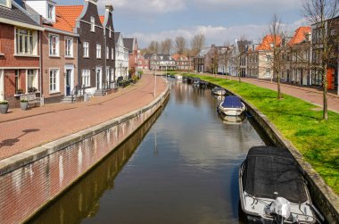 Maarssen, Hollanda, 9 Nisan 2023: Yeni bir mahallede kanal, şalgam ve kanal evleri, tuğla iskele ve çimenli yamaçlar