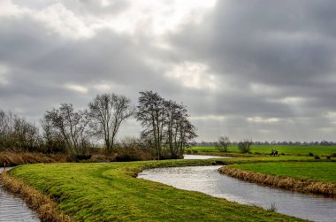Hollanda, Schoonhoven yakınlarında dramatik bir gökyüzü altında iki balıkçı ile kanallı ve çayırlı Polder manzarası
