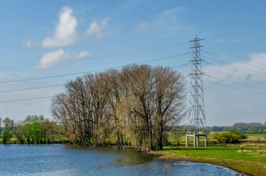Hollanda, Nijmegen yakınlarındaki Waal nehrinin taşkın ovalarında, güzel bir doğa rezervinde beton bir stile sabitlenmiş, çelik bir elektrik direğinin yapımı.