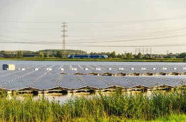 Zwolle, Hollanda, 8 Ağustos 2024: Arka planda elektrik direklerinin ve elektrik hatlarının yanı sıra Blauwnet tren hattının bulunduğu gölde yüzen güneş panelleri