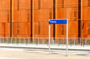 Tilburg, The Netherlands, September 10, 2024: platform sign with station name Tilburg, against the background of a corten steel parking garage facade clipart