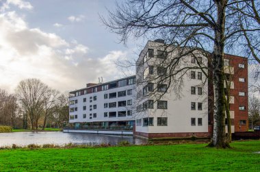 Rotterdam, Hollanda, 22 Aralık 2024: Banliyö parkındaki bir göletin yanındaki tuğla ve alçı kaplı bina