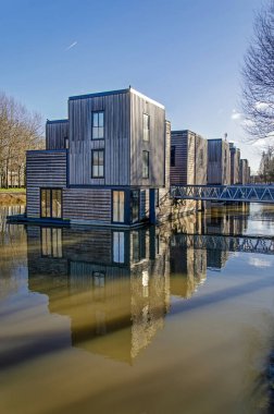 Rotterdam, 11 Ocak 2025: Kışın rüzgarsız ve güneşli bir günde eski bir liman temelinde yansıyan ahşap cepheli yüzer villalar.