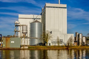 Lochem, Hollanda, 2 Şubat 2025: Kış mevsiminde mavi bir gökyüzünün altındaki bir kanalda siloların ve tankların bulunduğu sanayi sahnesi