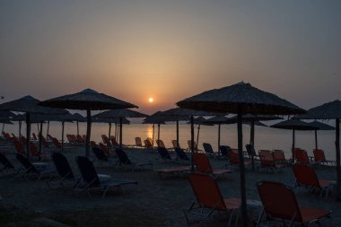 Plaj, şemsiyeler, güneş doğarken Paralia Katerini Yunanistan 'daki Ege Denizi üzerinde güneşlik yatakları