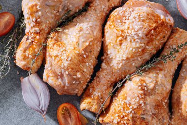 chicken drumsticks with spices, paprika and sesame seeds, ready to bake on a baking sheet