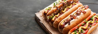 Koyu ahşap arka planda sarı Amerikan hardalıyla ızgara sosisli sandviç.