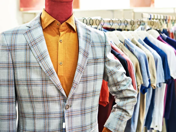 Men\'s plaid blazer on a mannequin and shirts on hangers in the clothing store