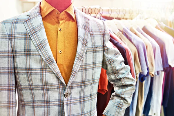 Men's plaid blazer on a mannequin and shirts on hangers in the clothing store