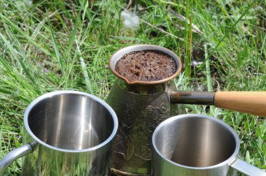 Kahve demlikten çimenlerin üzerinde bir fincana dökülüyor