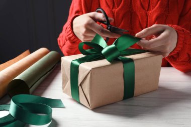Noel hediyesi. Beyaz ahşap masada hediye kutusunu dekore eden kadın, yakın plan.