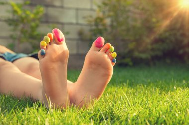 Yeşil çimlerin üzerinde boyalı ayak parmakları olan genç bir kız, yakın plan. Metin için boşluk