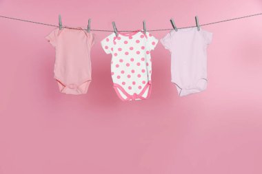 Bebek tulumları pembe arka planda çamaşır ipinde kuruyor.