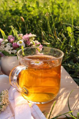 Bir fincan aromatik bitkisel çay ve seramik havan. Çayırdaki tahta üzerinde farklı kır çiçekleri var.