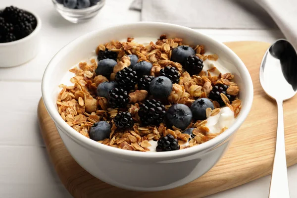 Bowl of healthy muesli served with berries on white wooden table, closeup