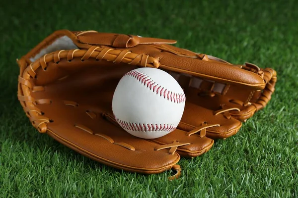 Catcher\'s mitt and baseball ball on green grass. Sports game