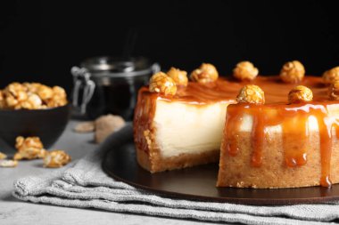 Sliced delicious cheesecake with caramel and popcorn on light grey table, closeup. Space for text