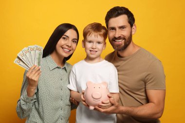 Seramik kumbarası ve turuncu arka planda parası olan mutlu bir aile.