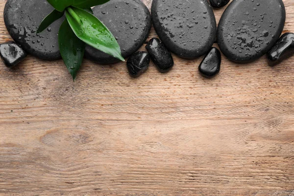 Wet spa stones and bamboo leaves on wooden table, flat lay. Space for text