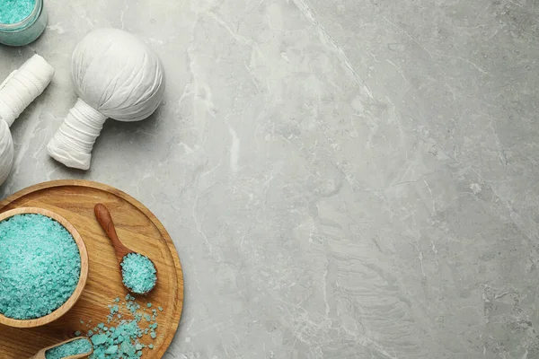Spa herbal bags and turquoise sea salt on grey marble table, flat lay. Space for text