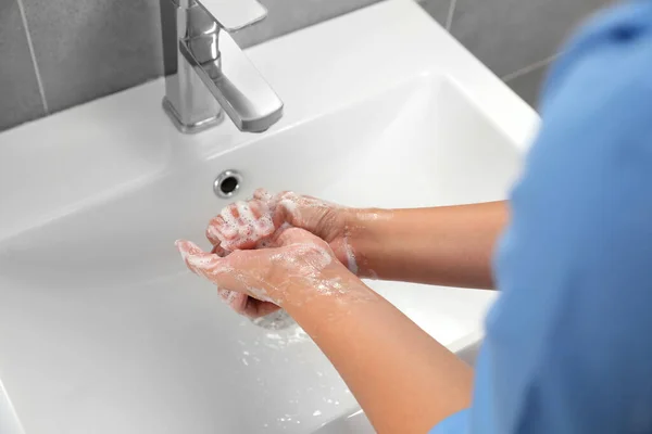 Doctor washing hands with water from tap in bathroom, closeup