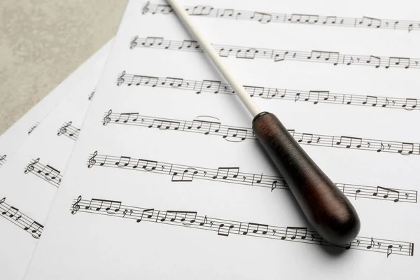 Conductor\'s baton and sheet music on grey background