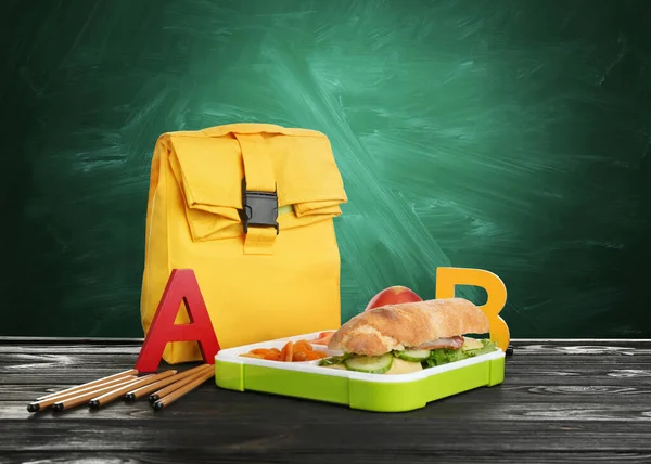 緑の黒板の近くのテーブルの上に食べ物や袋を食欲をそそる弁当箱 — ストック写真