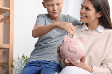 Çocuk annesiyle birlikte evdeki domuz kumbarasına para yatırıyor.