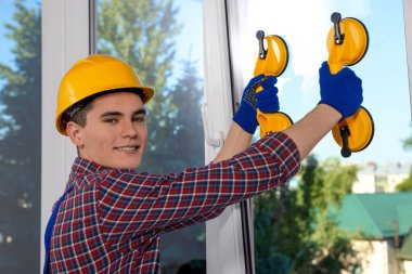 Worker using suction lifters during plastic window installation indoors