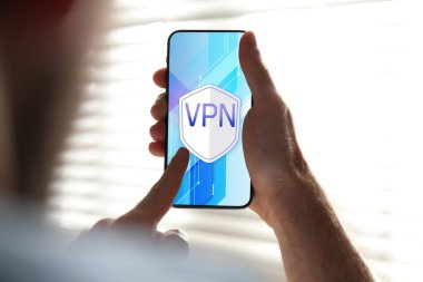 Akıllı telefonu kullanan bir adam kapalı alanda VPN 'i açmış, yakın plan.