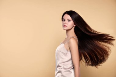 Bej arka planda sağlıklı ve güçlü saçları olan güzel genç bir kadının portresi.