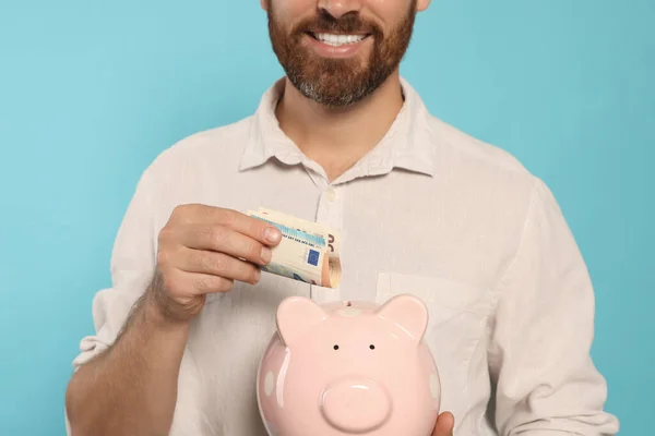 Щасливий Чоловік Вкладає Гроші Скарбничку Світло Блакитному Тлі Крупним Планом — стокове фото