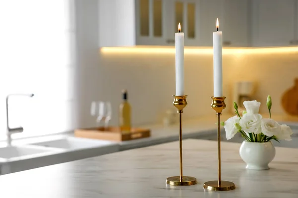 stock image Pair of beautiful golden candlesticks on white marble table in kitchen, space for text