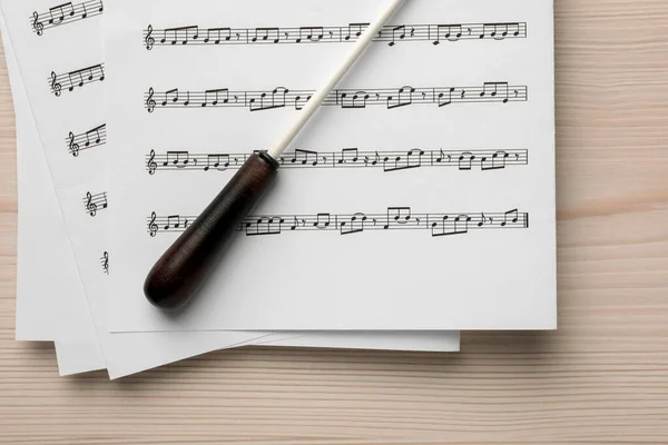 Conductor\'s baton and sheet music on white wooden table, top view