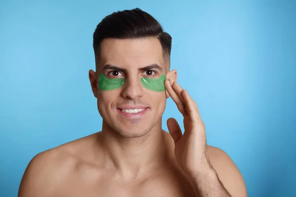 Mężczyzna Nakładający Zielony Plaster Pod Oczy Jasnoniebieskie Tło — Zdjęcie stockowe