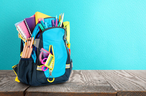 Рюкзак со школьными принадлежностями на деревянном столе против светло-голубой поверхности, место для текста