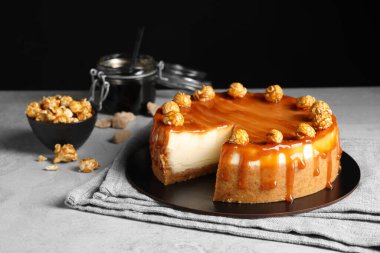 Dilimlenmiş lezzetli peynirli kek, karamel ve açık gri masada patlamış mısır.