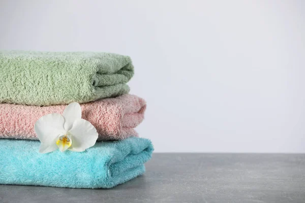 Stacked soft colorful towels with flower on grey table, space for text